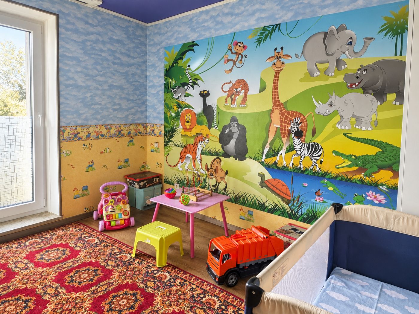 Spielzimmer mit Dschungel-Wandbild, Kindertisch und Laufgitter